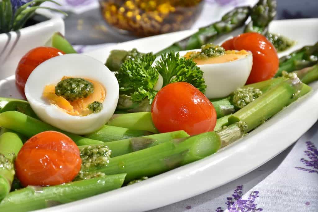 a plate of asparagus topped with tomatoes and boiled eggs