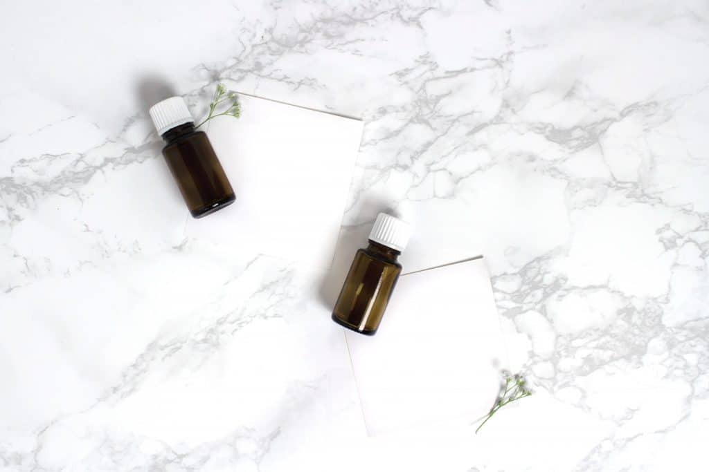 two bottles of detoxifying essential oils on a white marble background